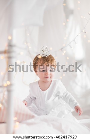 Cute toddler girl playing on a bed between warm soft Christmas lights