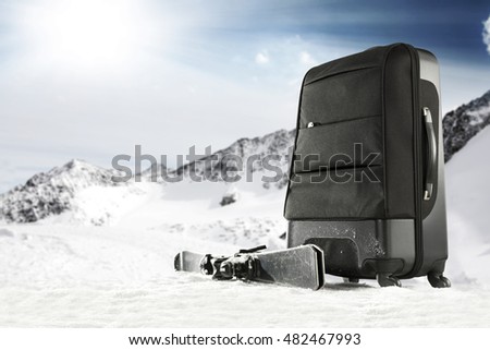 black suitcase on snow top and landscape of mountains 