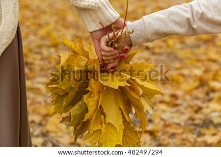 Autumn leaves.Mother and daughter walking in autumn park, holding hands with the bouquet of fallen leaves.