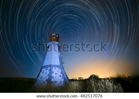 night photography tracks of stars on the background of the beautiful lighthouse. Starry beautiful sky in motion.
