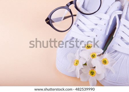 White stylish sneakers and flowers on light beige background. Modern glasses. With shadows. Side view. Place for your text.