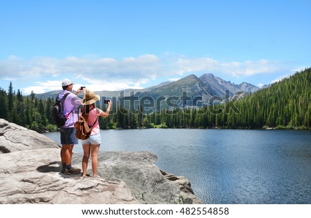 Family on hiking trip. Father and daughter taking photos of beautiful mountains with smart phones. Bear Lake Rocky Mountains National Park Colorado USA.