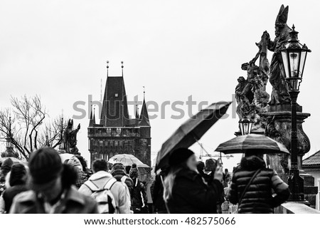 Tourists on Charles Bridge(Karluv Most) with Gothic architecture in the background, in a cold rainy day. BW photo. Prague, Czech Republic, Europe
