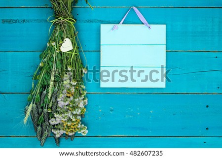 Bouquet of dried meadow flowers with heart and blank wood sign hanging by rope on antique rustic teal blue wood background; Mother's Day background with painted copy space