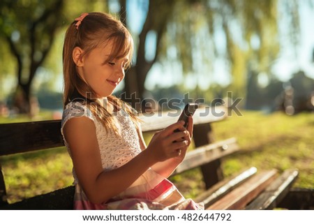 Cute and young girl sitting on a bench and using a mobile phone.