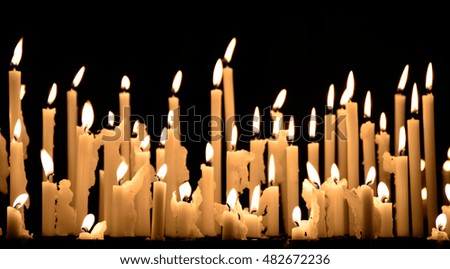 Yellow wax church candles burning in the dark. Copy space for text. Artistic blurry desaturated edit.