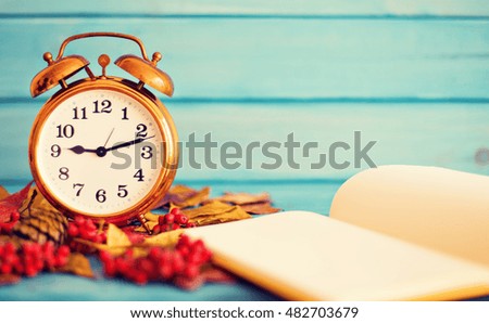 Vintage clock over autumn leafs and notebook