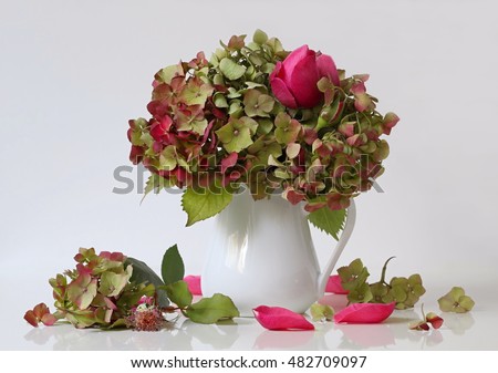 Autumn bouquet of green hydrangea flowers and pink roses in a vase  on a white background. Fall floral still life with hortensia and pink rose flowers, vase, petals and small florets. Home decoration.