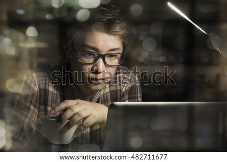 Young startup business working in office at night using tablet to analyze business information online, holding cup coffee, bokeh blurred city night light background. Horizontal, film effect.