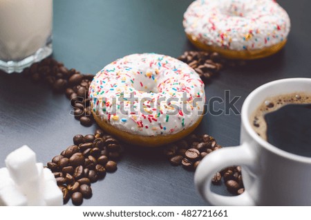 Donuts in a middle of picture. Coffee raw beans. Cup of coffee, sugar and milk. Breakfast on a dark blue table.