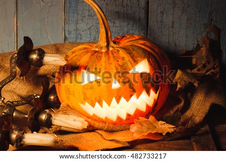 Halloween pumpkin with light from inside. Candle holder with candles and dry leaves on the wooden background