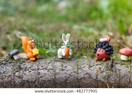 Plasticine world - little homemade squirrel with chanterelle, white bunny with a carrot and a hedgehog with mushroom sitting on a log, selective focus