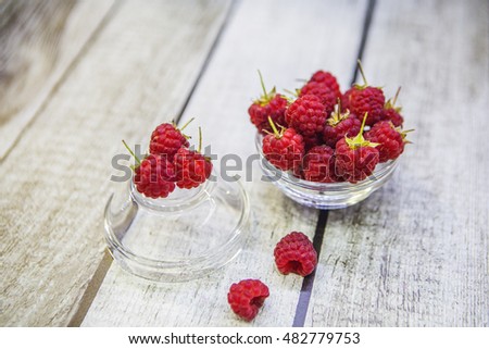 Raspberries in a glass vase on a wooden table.