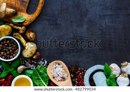 Organic vegetarian ingredients and fresh raw wild forest mushrooms for cooking on dark vintage background, top view, border, place for text.