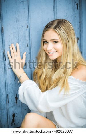 Teen girl poses for a high school senior portrait photo outdoors with wooden blue background