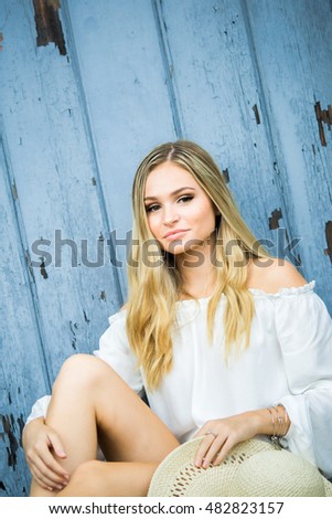 Teen girl poses for a high school senior portrait photo outdoors with wooden blue background