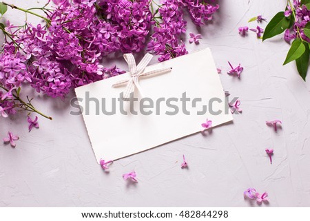 Violet lilac flowers  and empty tag on grey textured background. Selective focus. Place for text. Flat lay.