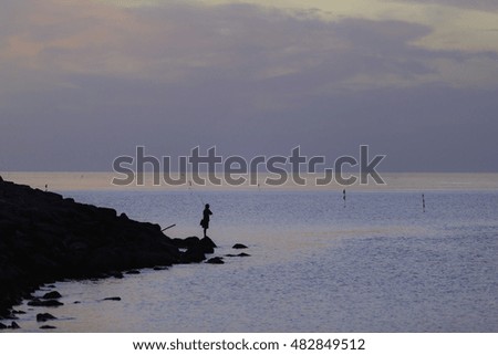 silhouette and soft focus picture of a fisherman with a fishing rod at the shore in sunrise