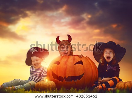 Happy brother and two sisters on Halloween. Funny kids in carnival costumes outdoors. Cheerful children and pumpkins on sunset background.