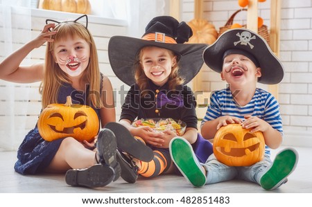 Happy brother and two sisters on Halloween. Funny kids in carnival costumes indoors. Cheerful children play with pumpkins and candy. Royalty-Free Stock Photo #482851483