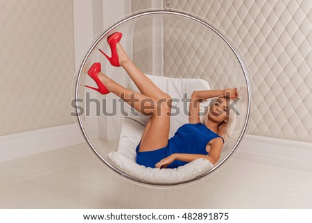The blonde in the studio.The blonde in blue dress and red shoes posing on the swing in the studio.