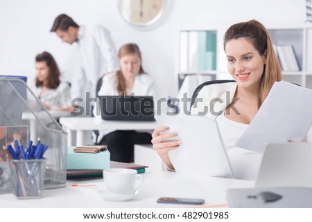 Pregnant office worker sitting beside desk and anlyzing documents