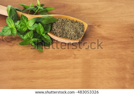 Basil leaves with spoon full of ground basil on a cutting board.