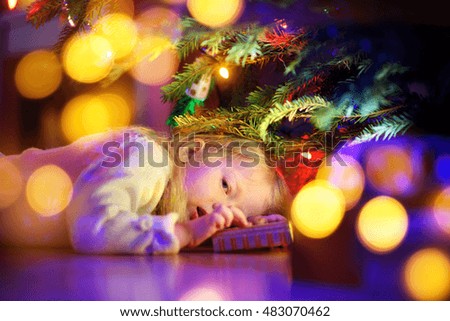 Adorable little girl looking for gifts under a Christmas tree on Christmas eve at home