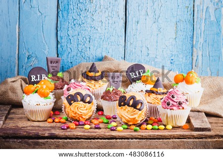 Halloween cupcakes with decorations: tombstone, eyes and pumpkins made from confectionery mastic, soft focus background
