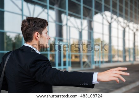 Young brunette businessman stopping car with hand outdoors