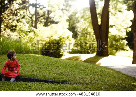 small and cute girl in a red dress sitting alone in the park