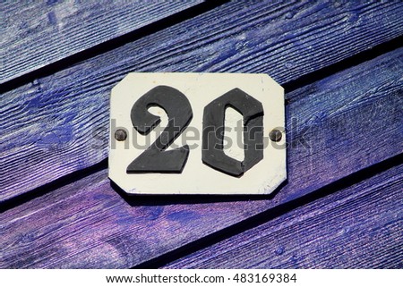 House number twenty. Black cypher on white fascia secured on woody deep purple wall.