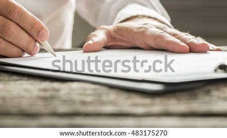 Man in white shirt signing business document or subscription form with silver pen on wooden desk. Low angle view.