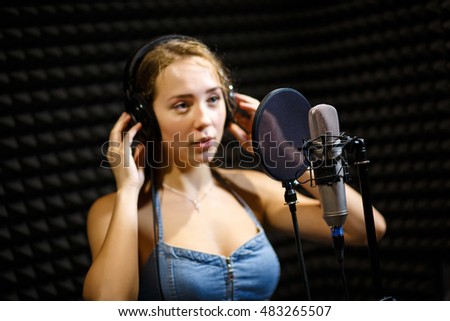 Portrait of beautiful female performer wearing headset singing song in recording studio.