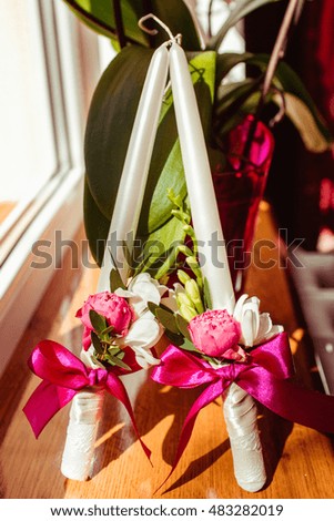 High white candles decorated with peonies stand on the windowsill