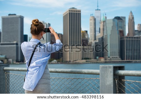 Tourist woman taking travel picture with camera of Manhattan Skyline and New York City skyline during autumn holidays. View from the back.
