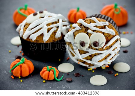 Halloween mummy cupcakes decorated with white chocolate on a stone table with sweet candy pumpkins selective focus