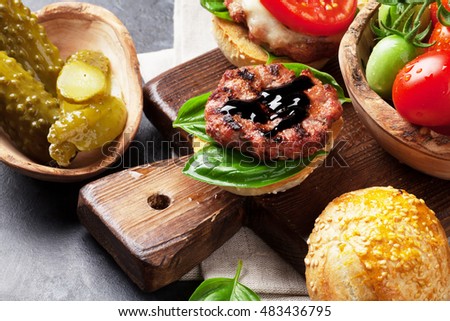 Homemade burgers with beef, cheese, tomatoes, cucumber and basil on cutting board