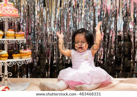 One-year old baby girl sitting on a table in front of her birthday cake.