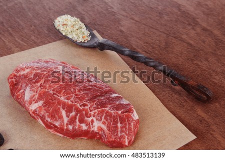 fresh raw beef rib eye steak on walnut table with salt spice and black iron antique forged cutlery fork knife