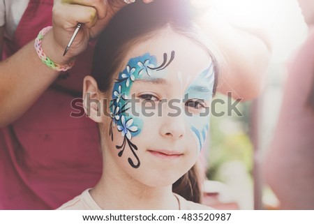 Child animator, artist's hand draws face painting to little girl. Child with funny face painting. Painter makes blue butterfly at girl's face. Children holiday, event, birthday party, entertainment.
