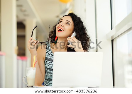 Smiling beautiful young woman using laptop and talking on the mobile phone.