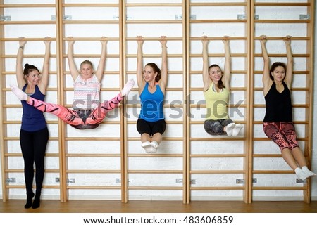 Group of young sports woman does an extension exercise at the Swedish wall