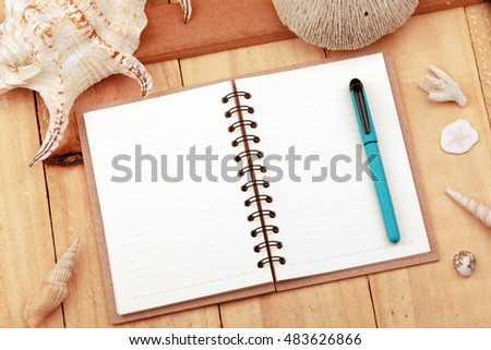 An empty, open note book with leather journal, pen and shells on a wooden desk top background