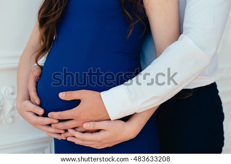 Belly of a pregnant girl in a blue dress. A man's hands and a woman's hands on a pregnant belly