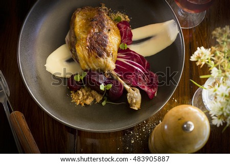 Roasted duck leg on a brown plate and wood table overhead