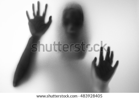 Horror woman behind the matte glass in black and white. Blurry hand and body figure abstraction.Halloween background Royalty-Free Stock Photo #483928405