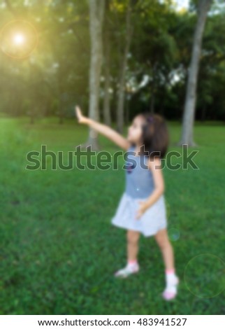 a blurred picture of little girl standing and pointing to bright light in park, filtered color tone