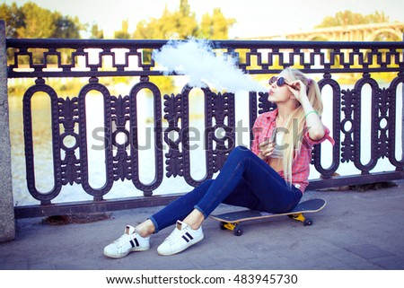 Elegant woman smoking e-cigarette with smoke, wearing suit and hat
