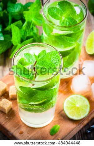 fresh mojito cocktails with lime, mint and ice in glass on wooden background